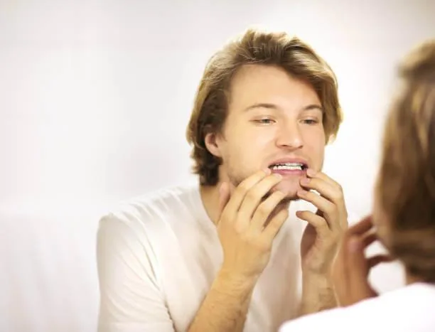 guy looking at his teeth in the mirror while deciding between teeth bonding or veneers to enhance his smile