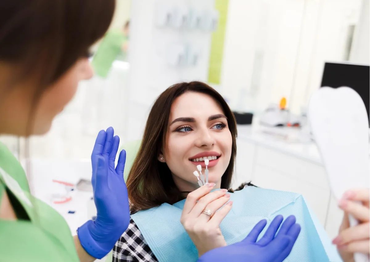 Patient comparing veneer shades during a consultation about preparing and covering teeth with veneers.
